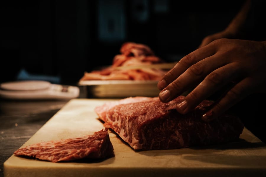 Hands trimming a well-marbled cut of beef on a wooden board in warm low light